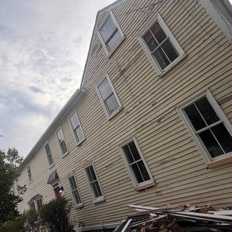 Clapboard siding scraped of loose paint, with removed trim on the ground.