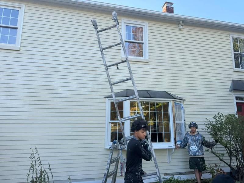 Two painters by a bay window with ladders against the cream siding.