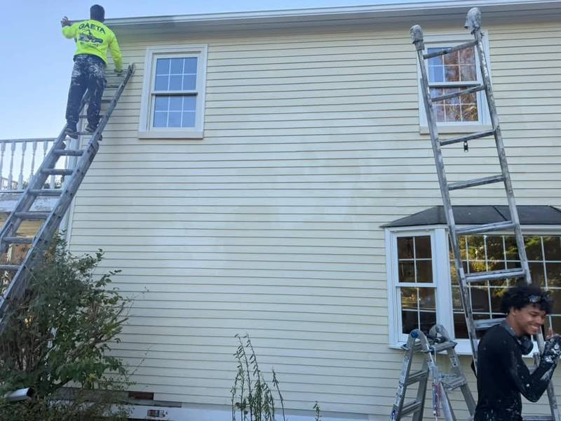 A painter on a ladder at the upper windows while another works below.