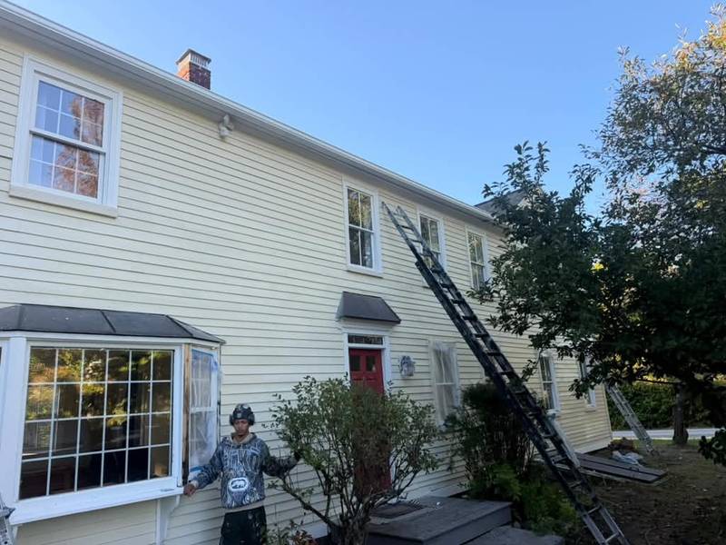 A painter beside a bay window with a ladder against the side of the house.