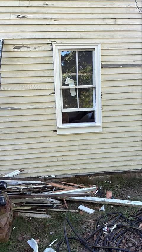 A window with new white trim on scraped siding, old trim on the ground below.