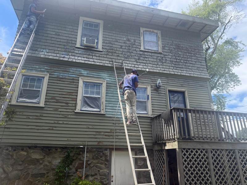 A painter on an extension ladder working on the clapboard of a three-story house.
