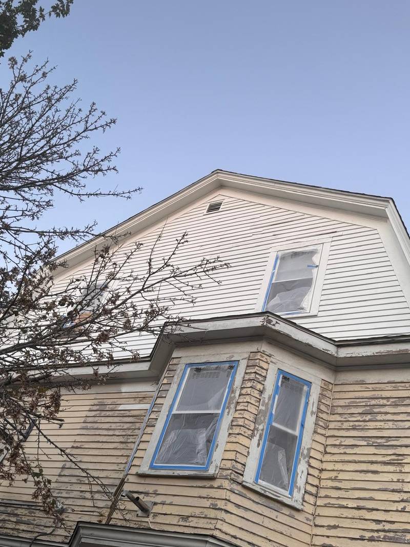 A gable and bay window with peeling paint before preparation.