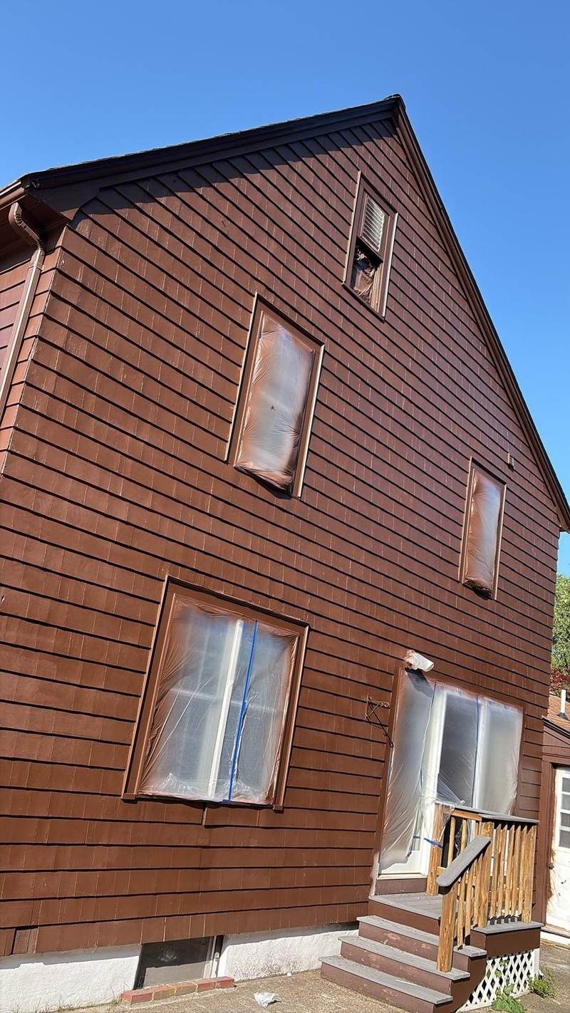 Red-brown clapboard siding freshly finished, with the windows still masked off.