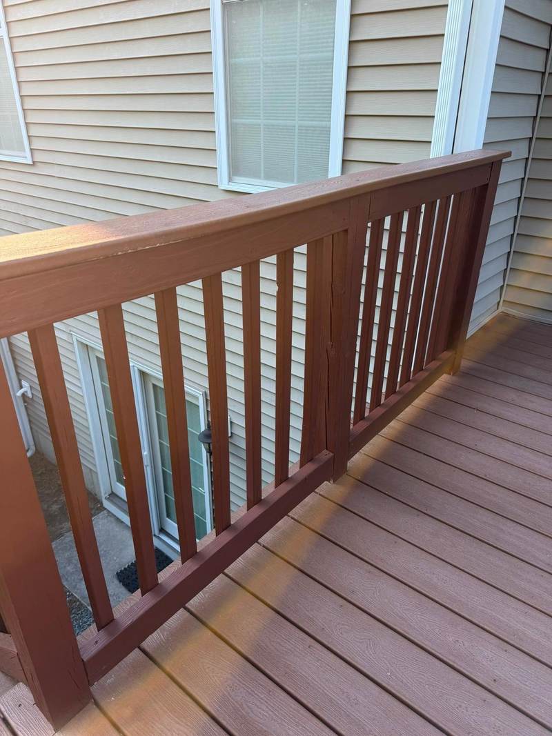 A deck railing and deck boards finished in brown stain against tan siding.