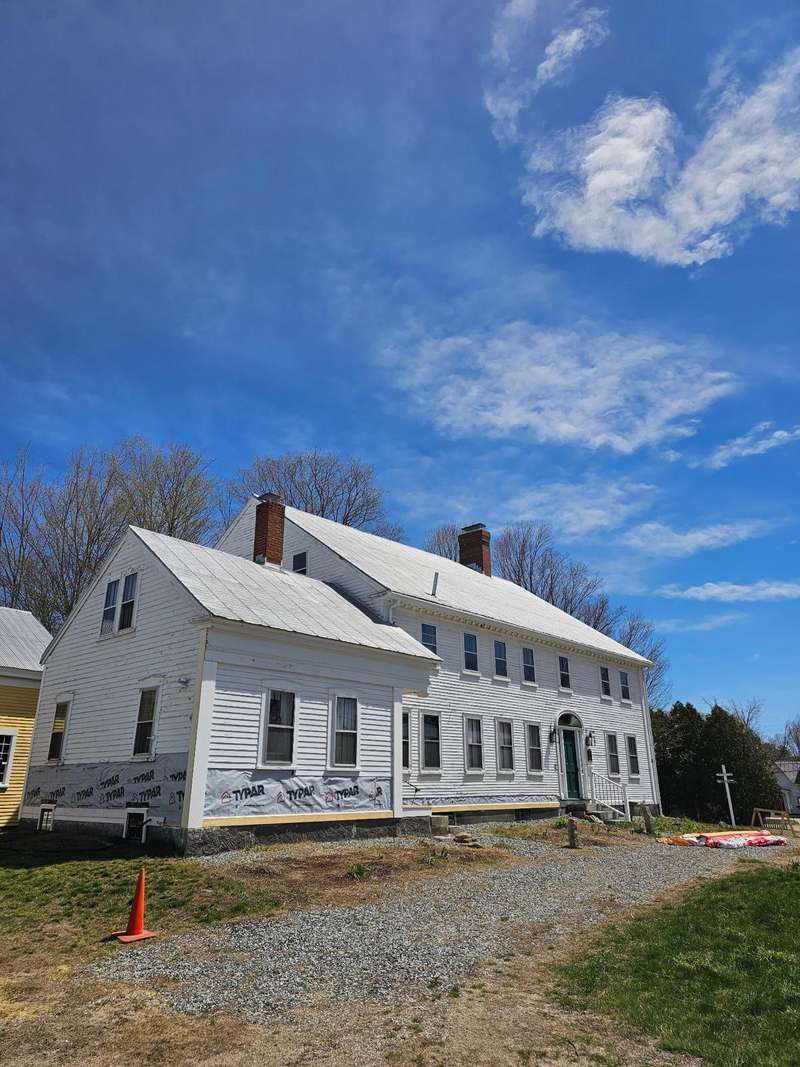 A long white farmhouse with a dark green door and two chimneys, photographed on site.