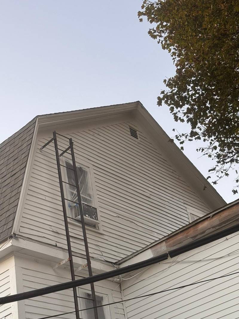 The gable of a white house with a ladder against it during preparation.