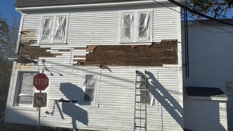 Close view of a white house with damaged siding stripped back to the boards.