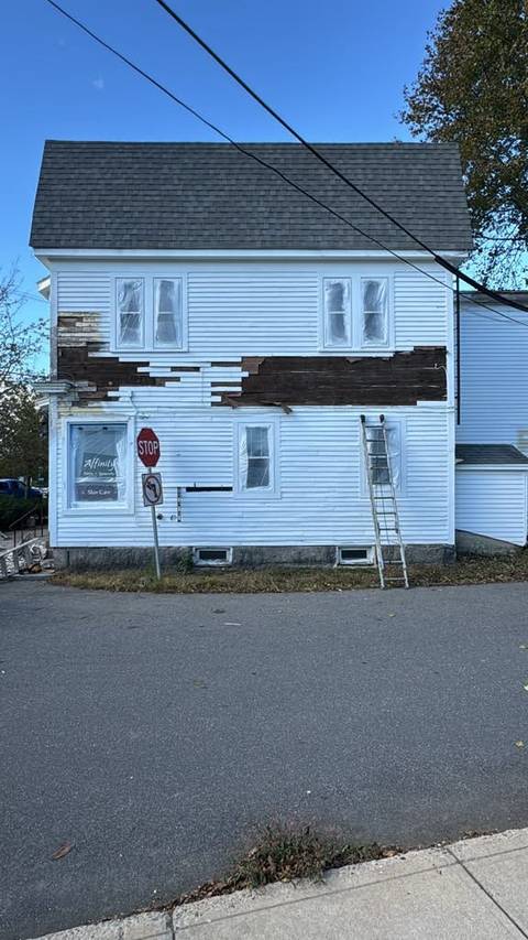 A white house with damaged siding removed for repair, ladder against the wall.