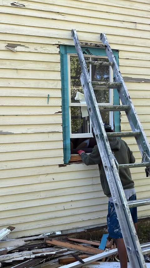 A window frame stripped to bare wood while trim is replaced, ladder alongside.
