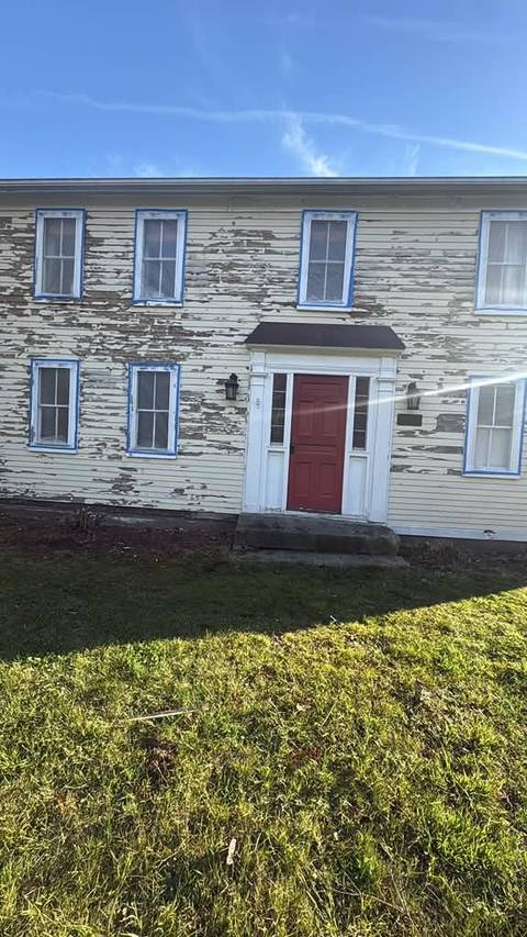 A two-story colonial with peeling pale yellow paint and a red door, before work began.
